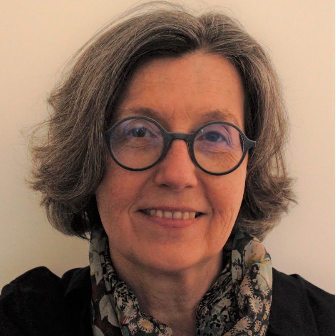 Doris-Schrocker - Fresh Thinking Labs Smiling woman with short gray hair and round black glasses, wearing a patterned scarf against a neutral background.