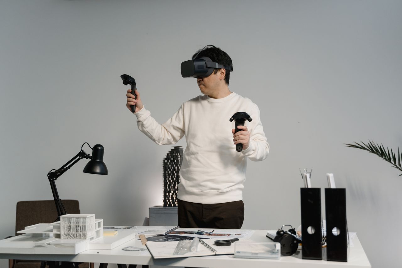 pexels-photo-6614749-6614749 Adult man in workspace using VR headset and controllers, engaging with virtual reality experience.