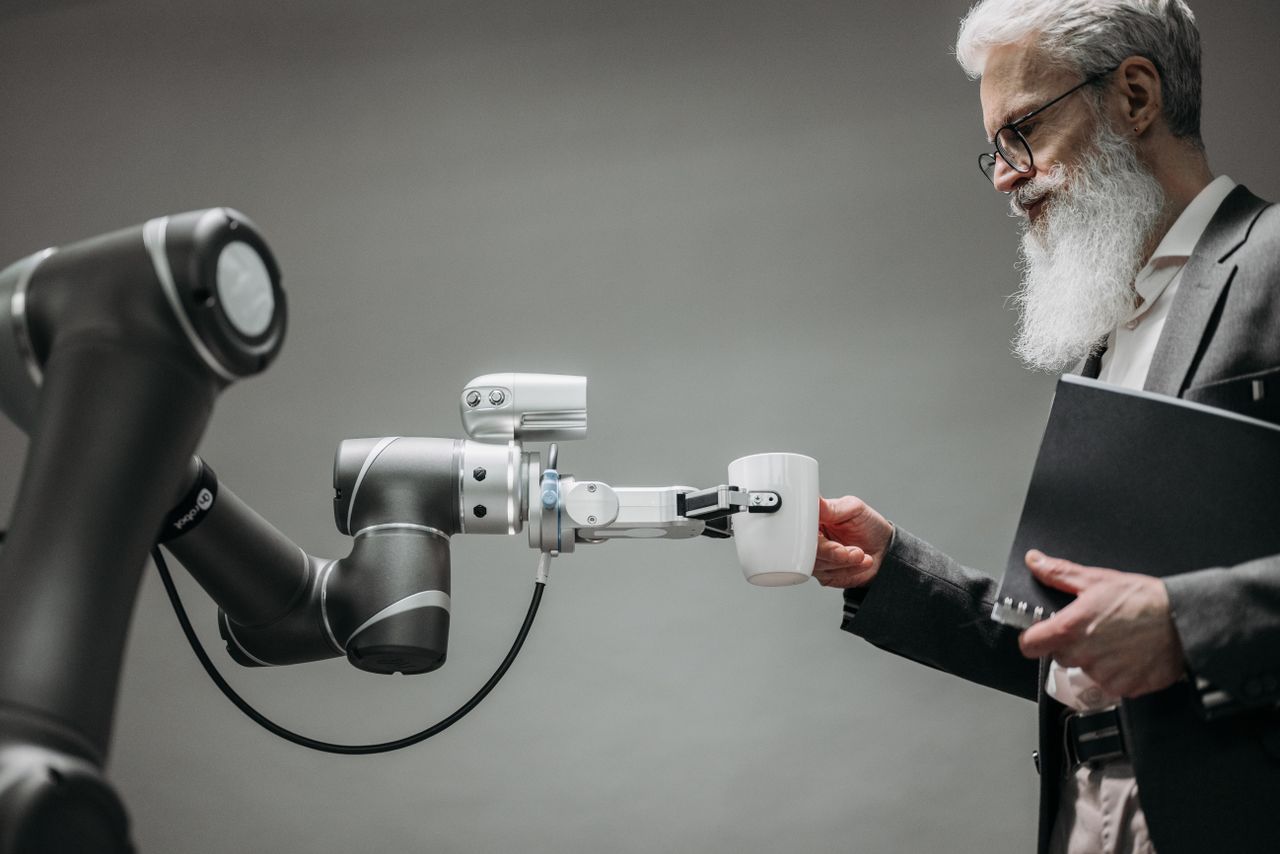 pexels-photo-8439093-8439093 An elderly man receives a cup from a robotic arm in a modern office setting.