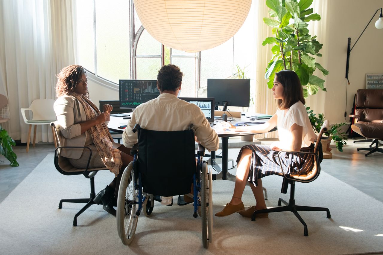 Diverse team having a discussion in a modern office setting with natural light. Includes a member using a wheelchair.